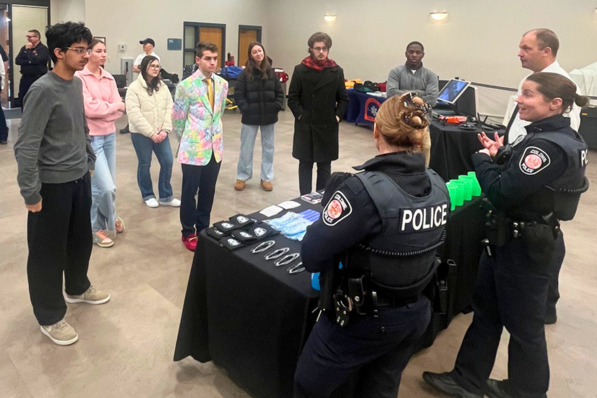 Students stand in a semi circle listening to people dressed in police uniforms speak